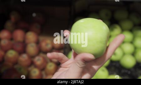 Frau wählt grüne Äpfel im Lebensmittelgeschäft in der Obst- und Gemüseabteilung. Frau nimmt Apfel auf und inspiziert ihn. Stockfoto