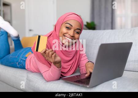 Einfaches Zahlungs- und Cashback-Konzept. Glückliche afrikanisch-amerikanische Dame beim Online-Shopping zu Hause über Laptop Stockfoto