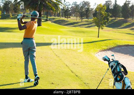 afroamerikanischer junger Mann, der im Sommer mit einem Golfclub auf dem Rasen auf dem Golfplatz Golf spielt Stockfoto