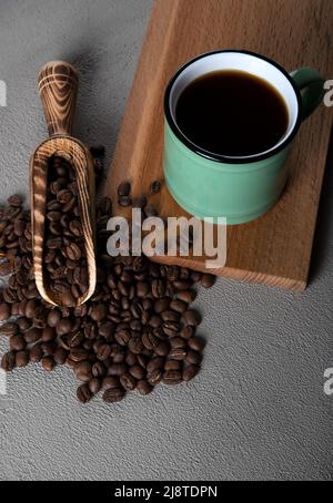 Grüne Tasse Kaffee mit Kaffeebohnen auf betonem Hintergrund Stockfoto