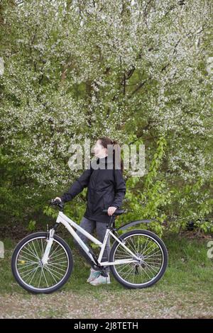 Frau mit dem Fahrrad unter einem blühenden Obstbaum im Park. Frühlingspicknick zur Entspannung Stockfoto