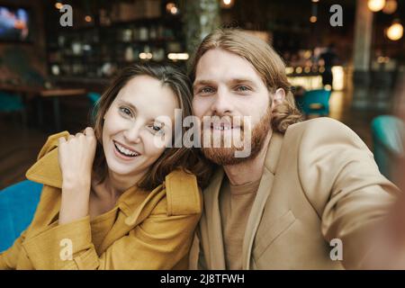 Unzufriedener junger bärtiger Mann, der im modernen Café sitzt und auf Antwort wartet, während er per Handy anruft Stockfoto