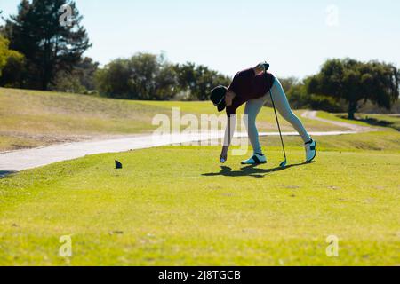 Die ganze Länge des kaukasischen jungen Mannes, der im Sommer den Golfball auf dem Abschlag auf dem Golfplatz hält Stockfoto