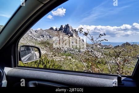Blick von einem Autofenster auf die Felsen und die spärliche Vegetation im Velebit-Gebirge, Kroatien, während eines Roadtrip Stockfoto