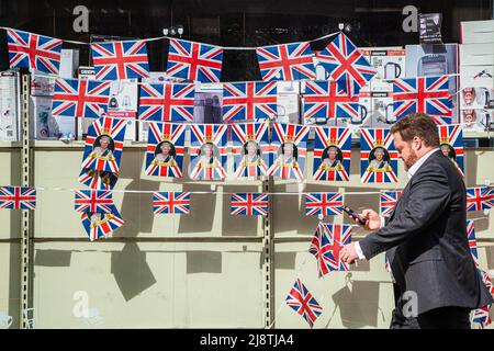 London, 18. Mai 2022. Eine Fußgängerin im Stadtzentrum von Wimbledon geht an einem Schaufenster vorbei, das mit Union Jack-Flaggen geschmückt ist und das Platinjubiläum feiert, da Königin Elizabeth 70 Jahre als die am längsten dienende britische Monarchie seit ihrer Thronbesteigung im Jahr 1952 feiert. Kredit. amer Ghazzal/Alamy Live Nachrichten Stockfoto