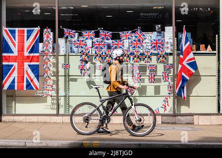 London, 18. Mai 2022. Eine Fußgängerin geht an einem Schaufenster im Stadtzentrum von Wimbledon vorbei, das mit Union Jack-Fahnen geschmückt ist und das Platinjubiläum feiert, da Königin Elizabeth 70 Jahre als die am längsten dienende britische Monarchie seit ihrer Thronbesteigung im Jahr 1952 feiert. Kredit. amer Ghazzal/Alamy Live Nachrichten Stockfoto