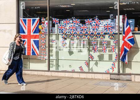 London, 18. Mai 2022. Eine Fußgängerin geht an einem Schaufenster im Stadtzentrum von Wimbledon vorbei, das mit Union Jack-Fahnen geschmückt ist und das Platinjubiläum feiert, da Königin Elizabeth 70 Jahre als die am längsten dienende britische Monarchie seit ihrer Thronbesteigung im Jahr 1952 feiert. Kredit. amer Ghazzal/Alamy Live Nachrichten Stockfoto