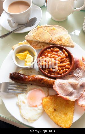 Café Mahlzeit ein kleines englisches Frühstück Speck Spiegelei Wurst gebackene Bohnen Hash braun und Weißbrot Toast und Butter und eine Tasse Tee in Yorkshi serviert Stockfoto