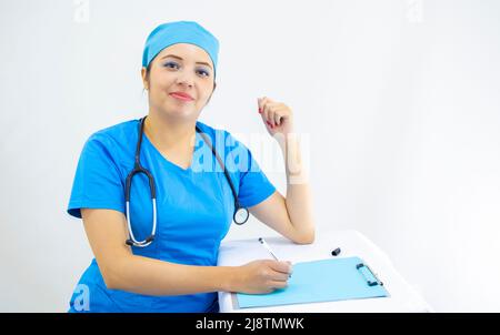 Schöne Frau Labortechnikerin trägt einheitliche und blaue OP-Kappe, die Ergebnisse analysiert, auf weißem Hintergrund Stockfoto