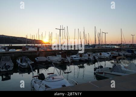 Viele weiße Yachten und private Vergnügungsboote, die in der Marina in der Stadt Koper in der Nähe des Stadtzentrums festgemacht sind. Im Horizont ist Landschaft und Sonnenuntergang. Stockfoto