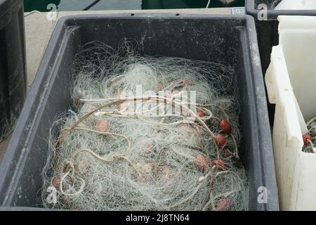 Fischernetz mit weißen Seilen und rot-braunen Schwimmern in schwarzer quadratischer Plastikbox gelagert, bereit zum Laden auf Fischerboot. Stockfoto