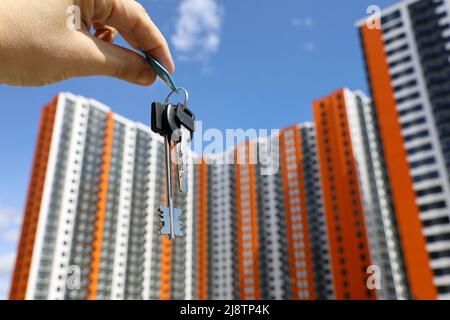 Hausschlüssel in männlicher Hand auf dem Hintergrund neuer Wohngebäude. Immobilienmakler, Umzug oder Vermietung von Immobilien Stockfoto