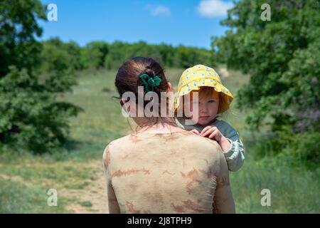 Eine Familie von Touristen geht durch die grünen Dickichte eines Frühlings-Bergwaldes. Mutter trägt eine schlafende kleine Tochter in ihren Armen. Wunderschön üppig Stockfoto