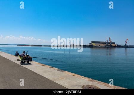 Seehafen in Burgas, Bulgarien. Foto des Anlegekai und der Hafenkrane an einem Sommertag. Fischer arbeiten in den Häfen vom Pier aus. Stockfoto