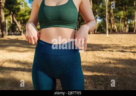 Kurze Aufnahme einer schlanken Frau mit flachem Bauch in grünem Sport-BH und blauen Leggings und Thema im Stadtpark im Freien. Gesundes Leben, im Freien Stockfoto