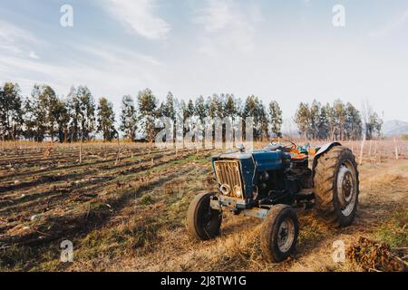 Breiter Schuss eines alten blauen Traktors mitten auf dem Ackerland. Stockfoto