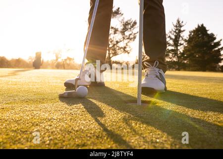 Niedriger Abschnitt eines kaukasischen jungen Mannes mit Schläger, Ball und flagstick in einem Loch auf dem Golfplatz Stockfoto