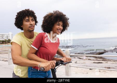 Liebende junge afro afroamerikanische Paar genießen Push Scooter Fahrt am Strand, kopieren Raum Stockfoto