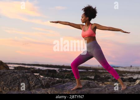 Junge afro-afroamerikanische Frau mit ausgestreckten Armen beim Training am Strand während des Sonnenuntergangs Stockfoto