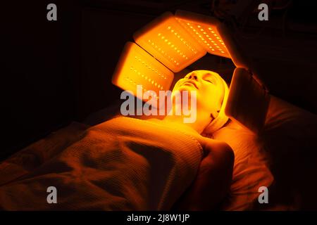 Eine ältere Frau durchläuft eine Gesichtsverjüngung. Frau Gesicht lt Rotlichtbehandlung in der Schönheitsklinik. Kosmetologie. Stockfoto