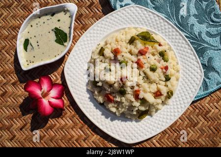 UPMA Indisches Grießfleisch Frühstück gesundes Gericht mit weißem Kokosnuss-Chutney serviert. Draufsicht auf Gemüse-Upama auf einer Wicker-Bambusmatte Stockfoto