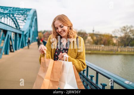 Schöne glückliche junge blonde Frau posiert mit Öko-Papiertüten draußen lachen, während Sie auf der Stadt zu Fuß Stockfoto