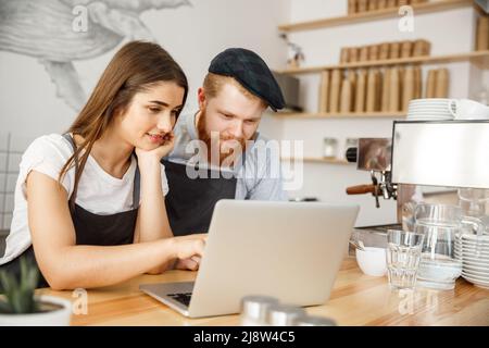 Kaffee Geschäftskonzept - Zufrieden und lächeln Besitzer Blick auf Laptop für online Bestellungen im Coffee Shop Stockfoto