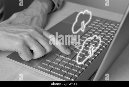 Cloud-Computing. Mann mit Laptop zum Herunterladen von Dateien aus dem Online-Speicher. Nahaufnahme des Zeigefingers durch Drücken der ENTER-Taste. Schwarz und Weiß. Hochwertige Fotos Stockfoto