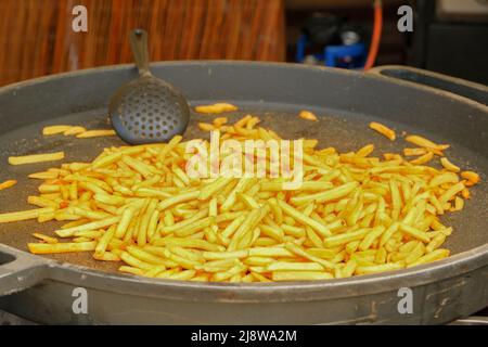 Bratkartoffeln in einer großen gusseisernen Pfanne. Straßenlokal. Kartoffeln in großen Töpfen braten. Stockfoto