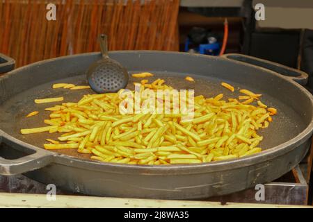 Bratkartoffeln in einer großen gusseisernen Pfanne. Straßenlokal. Kartoffeln in großen Töpfen braten. Stockfoto