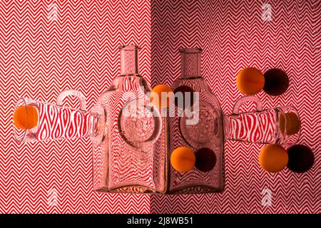 Abstraktes Stillleben mit Glaswaren und Kugeln auf einem roten geometrischen Hintergrund Stockfoto