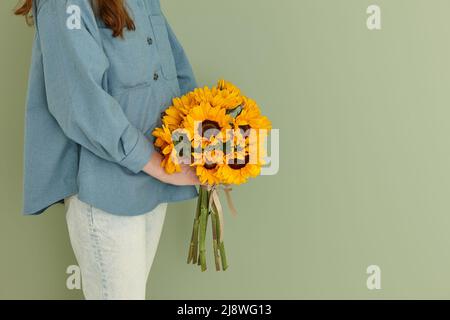 Frau mit einem Sommerstrauß Sonnenblumen auf grünem Wandhintergrund Stockfoto