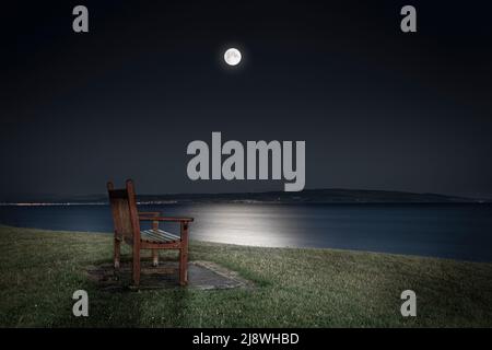 Öffentliche Bank mit Fernblick über das Meer im Mondlicht in der Nähe des Troon Pier, East Ayrshire, Schottland, Großbritannien Stockfoto