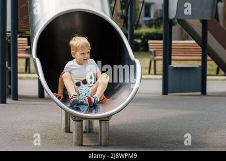 Netter Junge sitzt entspannt in der Röhre auf dem Spielplatz. Stockfoto