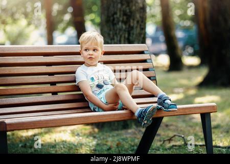 Netter Junge, der auf einer Bank im Park sitzt und sich ausruhen kann. Stockfoto