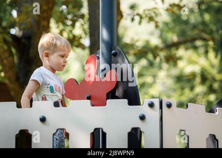 Spielen Boot Kapitän Junge, stehen am roten Helm oder Lenkrad des Schiffes auf dem bunten Spielplatz. Stockfoto