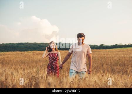Verliebte Paare verbringen romantische Zeit im Weizenfeld. Schöne glückliche Menschen, die draußen zusammen spazieren. Familientag. Sonniger Sommertag. Hände halten. Stockfoto