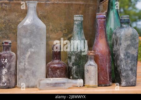 Nahaufnahme von alten, ausgegrasten Alkohol- und Medikamentenglasflaschen vor einem verrosteten Metallbehälter-Hintergrund. Stockfoto