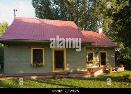 Altes, ca. 1840 kanadisches Blockhaus im Landhausstil, olivgrün gestrichen, mit gelben Zierleisten und kastanienbraunen Blechdach. Stockfoto