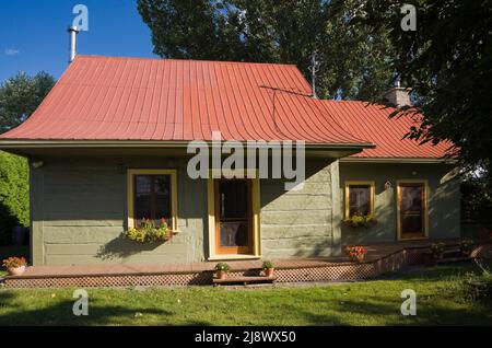 Altes, ca. 1840 kanadisches Blockhaus im Landhausstil, olivgrün gestrichen, mit gelben Zierleisten und kastanienbraunen Blechdach. Stockfoto