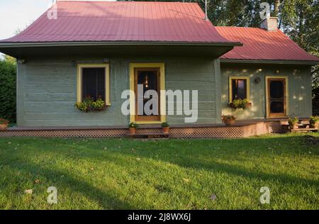 Altes, ca. 1840 kanadisches Blockhaus im Landhausstil, olivgrün gestrichen, mit gelben Zierleisten und kastanienbraunen Blechdach. Stockfoto