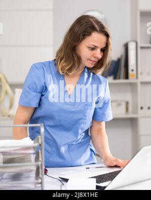 Porträt einer Ärztin, die mit Laptop und Dokumenten arbeitet Stockfoto