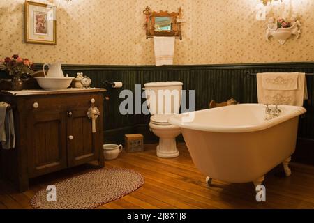 Freistehende Badewanne mit freistehender Fußspitze, Holzwaschtisch im Badezimmer im alten Steinbruch-Haus aus dem Jahr 1831 von Canadiana. Stockfoto