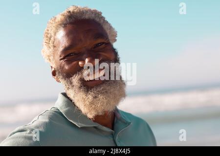 Nahaufnahme eines fröhlichen bärtigen afroamerikanischen Senioren, der im Sommer gegen Meer und blauen Himmel steht Stockfoto