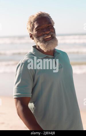 Porträt eines bärtigen glücklichen afroamerikanischen Senioren, der im Sommer gegen Meer und klaren Himmel steht Stockfoto