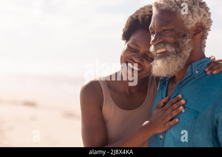Fröhlicher bärtiger afroamerikanischer Seniorchef und reife Frau mit afro-Haaren genießen am Strand Stockfoto