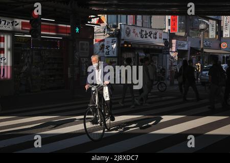 Tokio, Japan. 18.. Mai 2022. Ein Mann mit Gesichtsmaske fährt mit seinem Fahrrad über eine Fußgängerüberführung in der Nähe der U-Bahnstation Shin-?kubo in Tokio. Kredit: SOPA Images Limited/Alamy Live Nachrichten Stockfoto