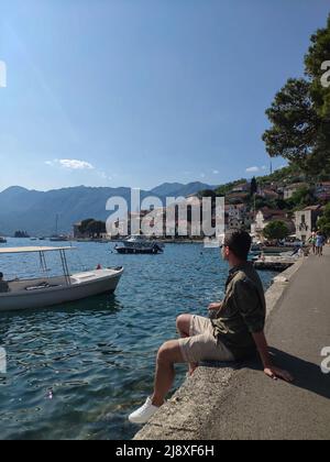 Der Mann sitzt und blickt auf das Stadtbild in der Altstadt von Perast, Montenegro Stockfoto