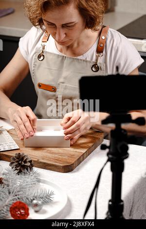 Frau, die handgemachte Pralinen herstellt und Inhalte für soziale Medien erstellt. Live-Übertragungen von der Kamera eines mobilen Smartphones eines Masterclass auf mak Stockfoto