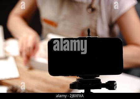 Frau, die handgemachte Pralinen herstellt und Inhalte für soziale Medien erstellt. Live-Übertragungen von der Kamera eines mobilen Smartphones eines Master Clas Stockfoto